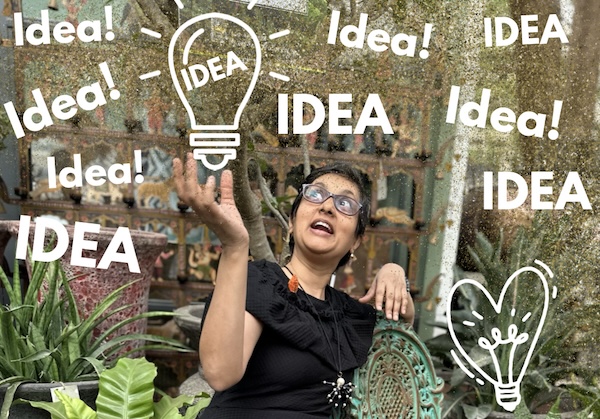 Short haired Indian lady in black dress, Susmitha, sitting on a garden chair and looking up. Hand reaching upwards. The word "Idea" printed several times overhead. One in a graphic light bulb. A representation of shiny object syndrome.