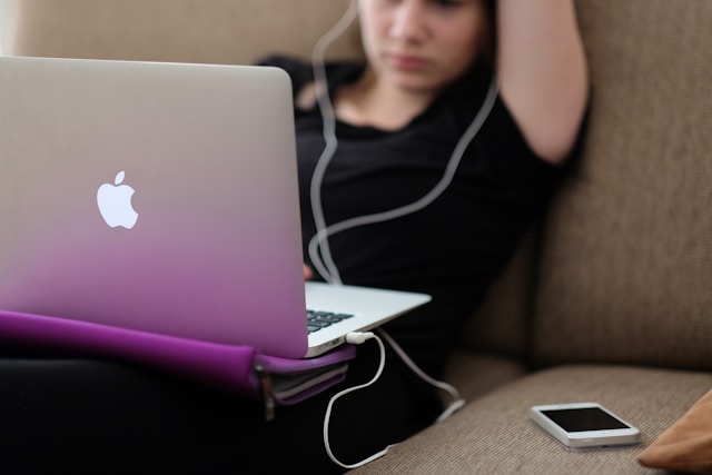 Lady in black clothes slumped on sofa staring at macbook pro on her lap, wearing earphones. Procrasta-learning. Procrastilearning.