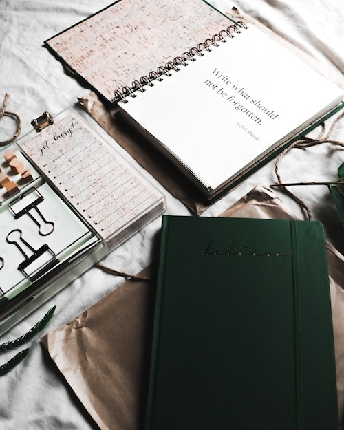 Open notebook on a table, with the quote "Write what should not be forgotten" on the first page. Tiny notebooks, and other fun stationery around it.