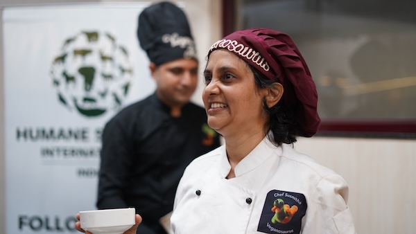 Chef Susmitha Veganosaurus in a cooking workshop. Smiling, fulfilled, joyful. Chef Ram and HSI logo in the background. Full potential or fulfilment?