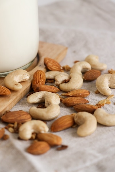 Cashews and almonds next to a glass bottle of plant based nut milk.