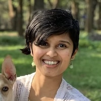 Supriya, in a park, smiling wide. Wearing a white top.