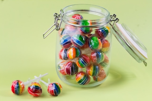 Colourful lollipops in a glass jar. On green surface.