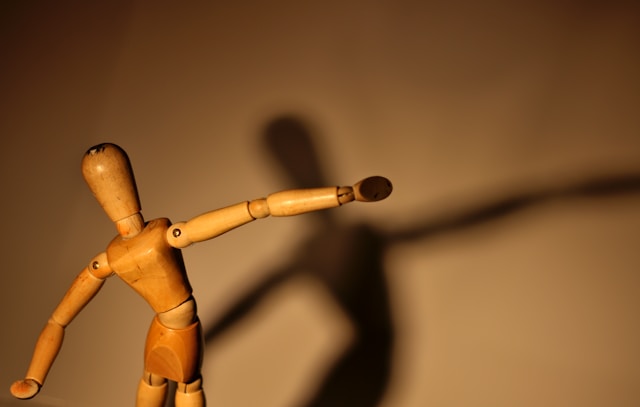 Wooden toy stretches out, shadow on wall. Imitating without understanding.