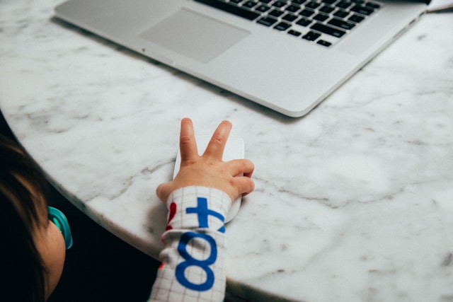 Tiny toddler hand reaching across a marble table top towards an open laptop. Doing things because she sees other doing it.