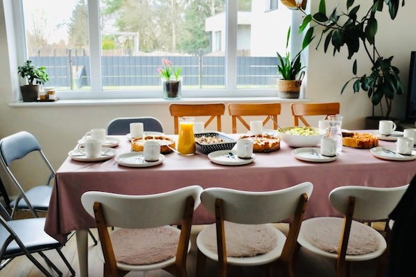 Table for eight set for a vegan pop-up meal. Brightly lit room, window and indoor plant in the background.